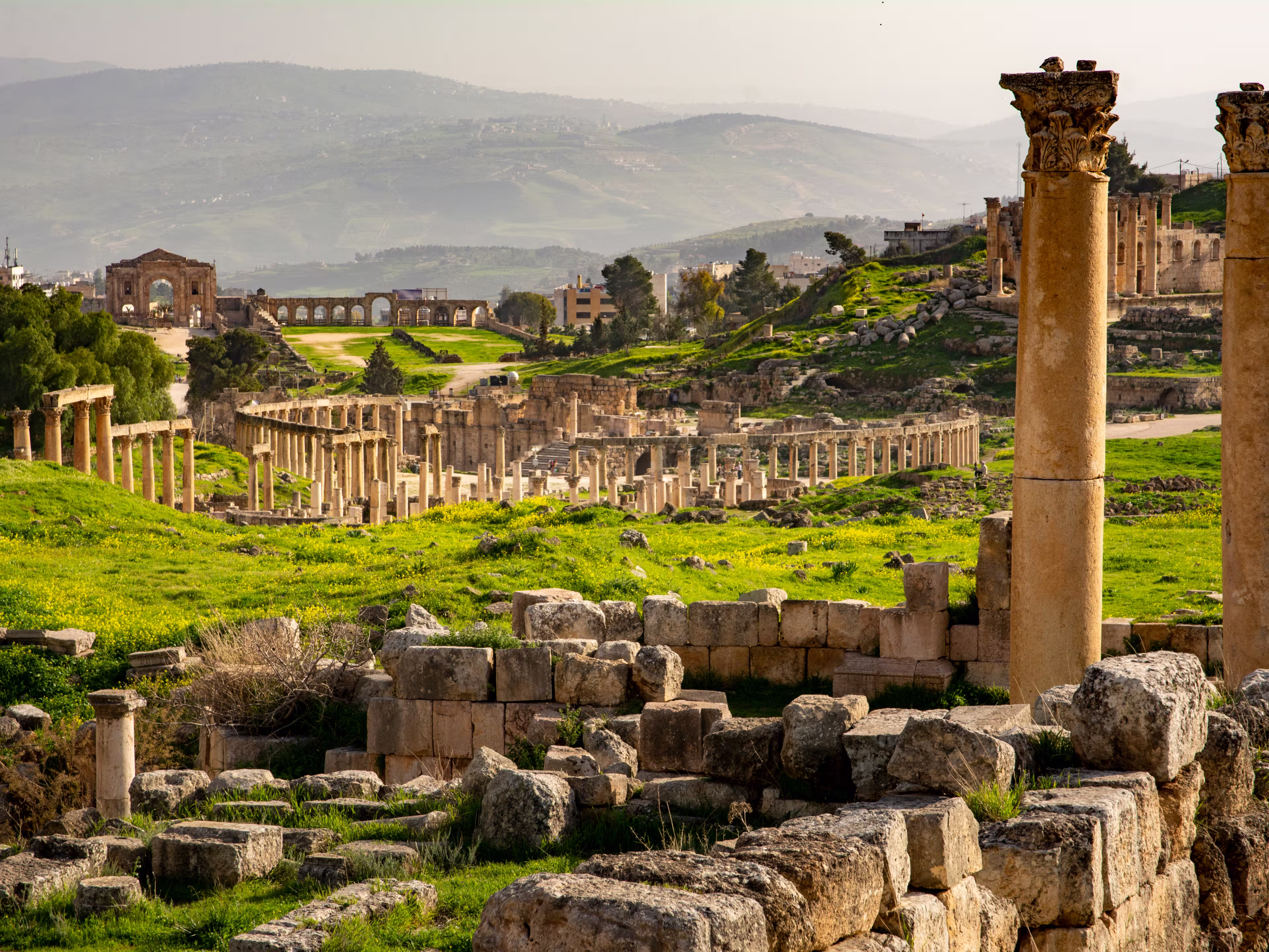 General view of the historical Roman site Gerasa in Jerash, Jordan, with pillars and Oval Plaza. Mountains and city in the far distance
