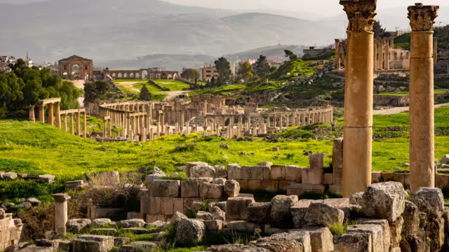 General view of the historical Roman site Gerasa in Jerash, Jordan, with pillars and Oval Plaza. Mountains and city in the far distance