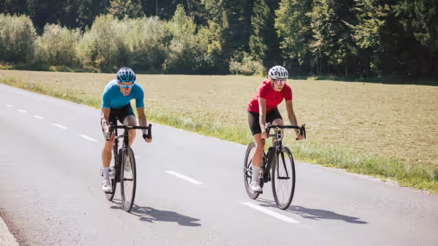 Two professional cyclist racers, male and female during training on a paved road through the mountain landscape, front view.