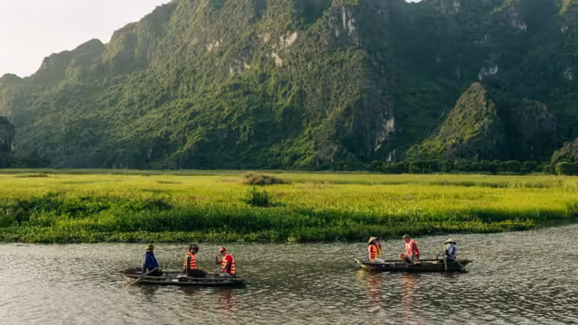 Wide shot of travellers and leader being guided on rowboats in the wide river valley of Van Long Nature Reserve