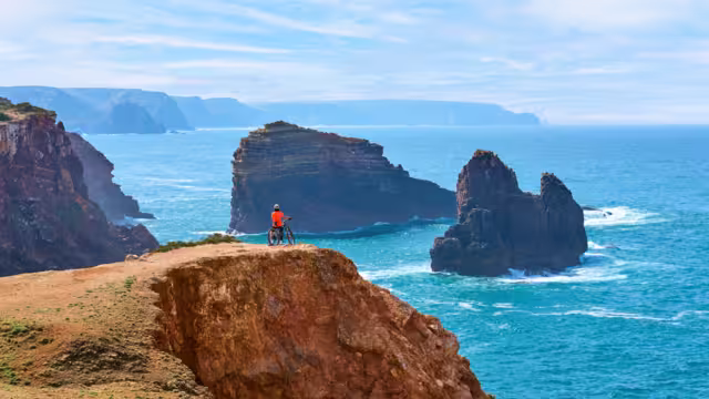 happy active senior woman cycling on the the rocky cliffs of the Vicentina coast of  Portugal near Sagres and Vila do Bispo
