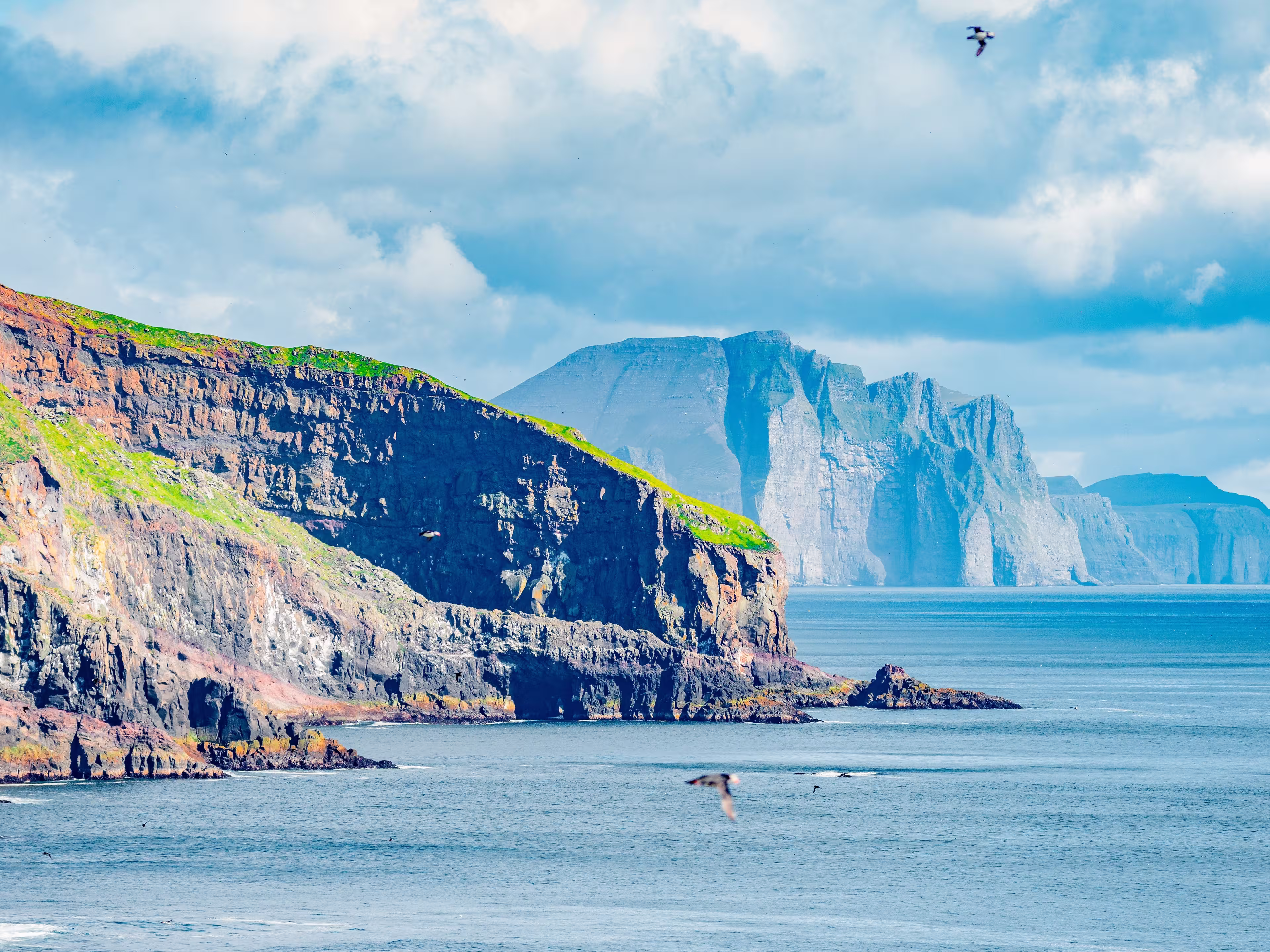 Mykines, Faroe Islands. Panoramic view of Mykines island, bird watching destination for puffins. Fjords landscape and seascape with flying puffins