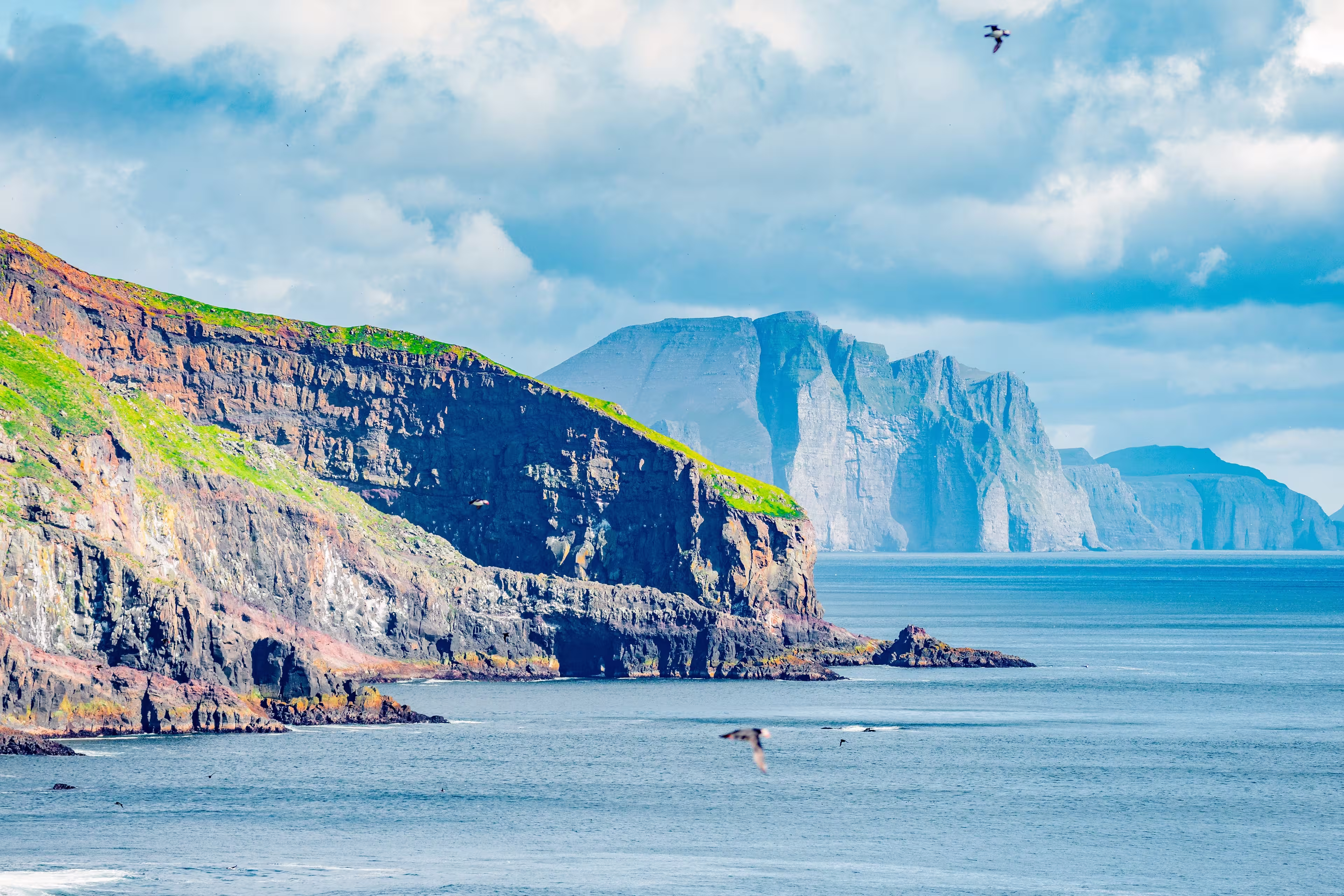 Mykines, Faroe Islands. Panoramic view of Mykines island, bird watching destination for puffins. Fjords landscape and seascape with flying puffins