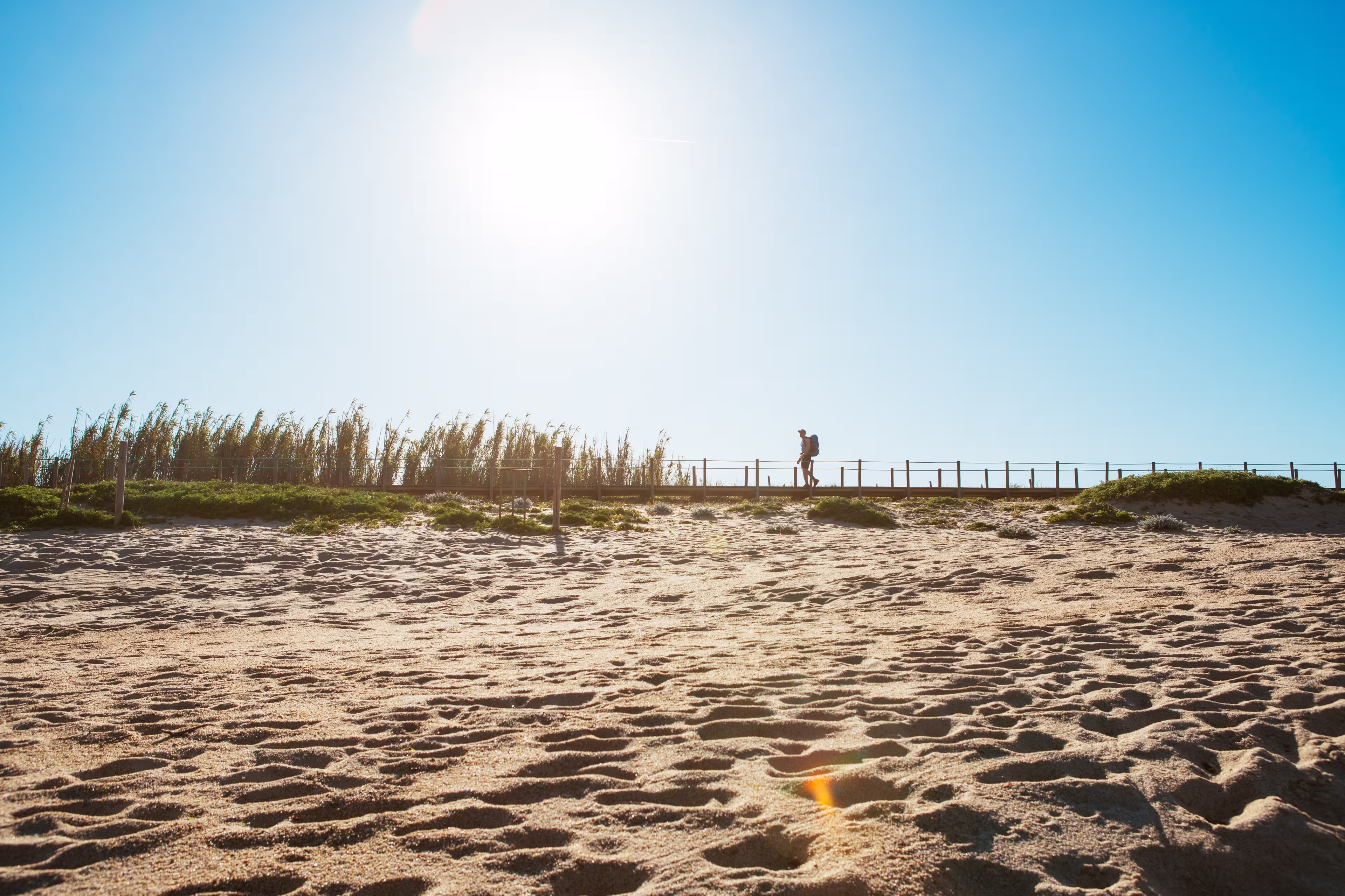 Lonely backpacker man walking by sandy Portugese beach in morning. Path leading by wooden passadicos  - boardwalks along the ocean coast. Shot during the Camino Portuguese —  popular pilgrimage route