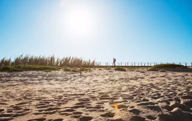 Lonely backpacker man walking by sandy Portugese beach in morning. Path leading by wooden passadicos - boardwalks along the ocean coast. Shot during the Camino Portuguese — popular pilgrimage route