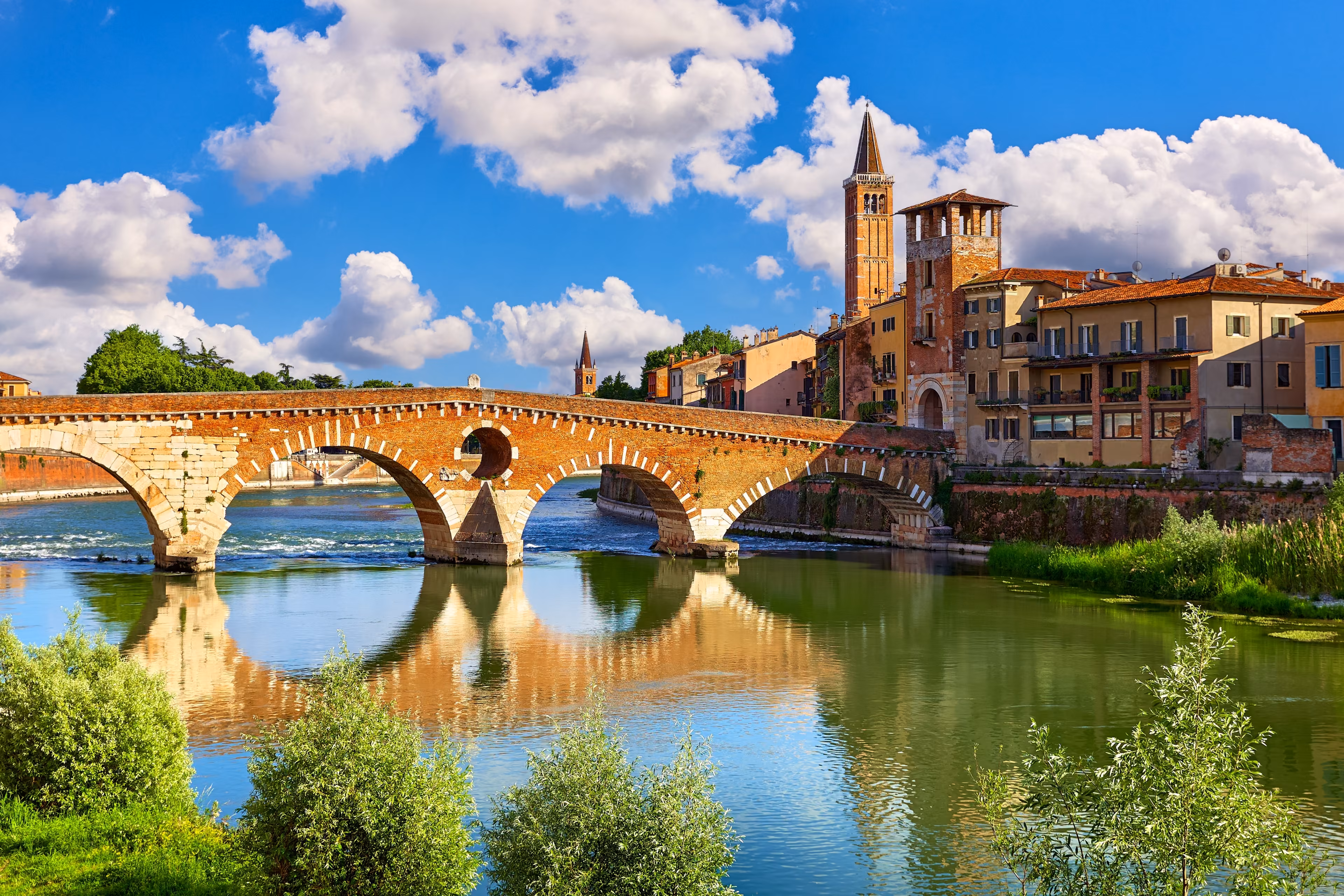 Verona, Veneto Region, Italy. Panoramic view at Bridge Ponte Pietra on Adige river. Sunny summer day panorama and blue sky with clouds. Ancient italian terracotta color houses.