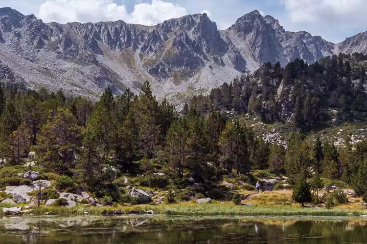 Wide shot of the Pyranees Mountains with green trees on hillside and a lake in the foreground