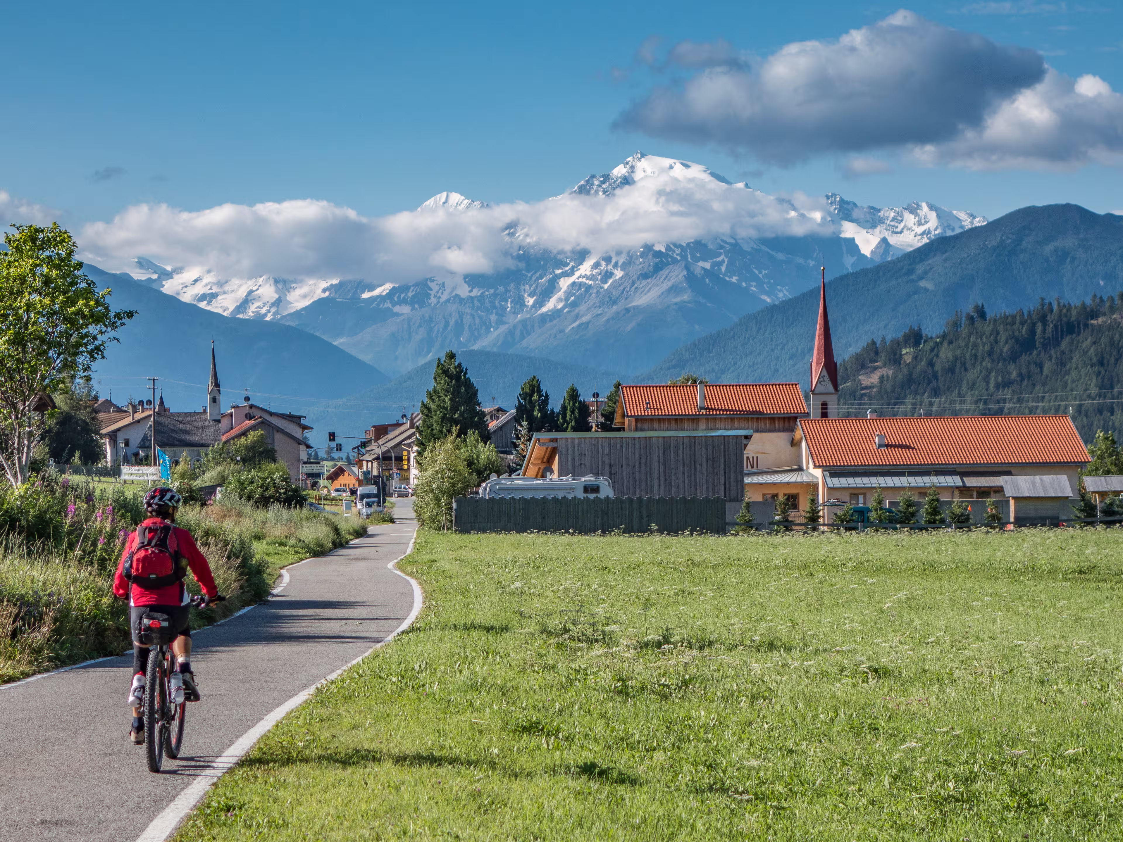 senior woman under way with her e-bike on the famous bicycle route Via Claudia Augusta, Alto adige,Italy, Mount Ortler in the background