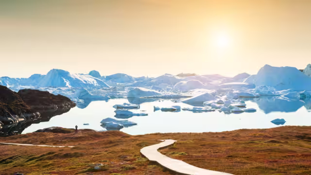 Traveller marvels and takes a photo at sunset on Disko Bay looking ta the Ilulissat Fjord on a trai in Greenland