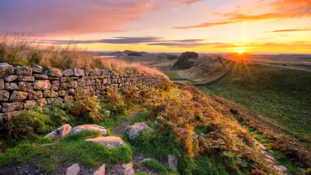Vibrant summer sunrise at Hadrians Wall overlooking Cuddy's Crags as the sun comes over the horizon. Northumberland, UK.