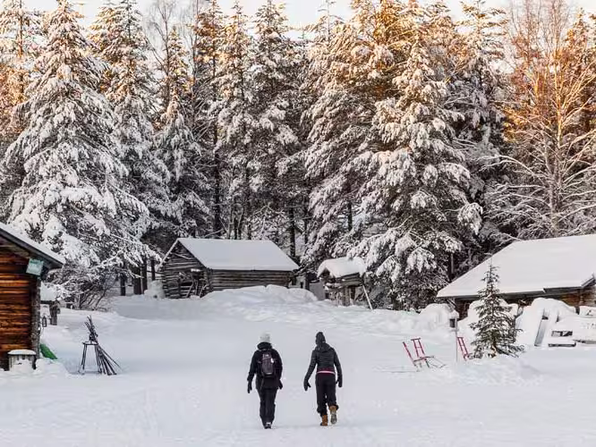 Two travellers walk through thick snow to get to cabin in Finland