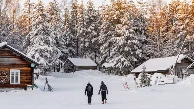 Two travellers walk through thick snow to get to cabin in Finland