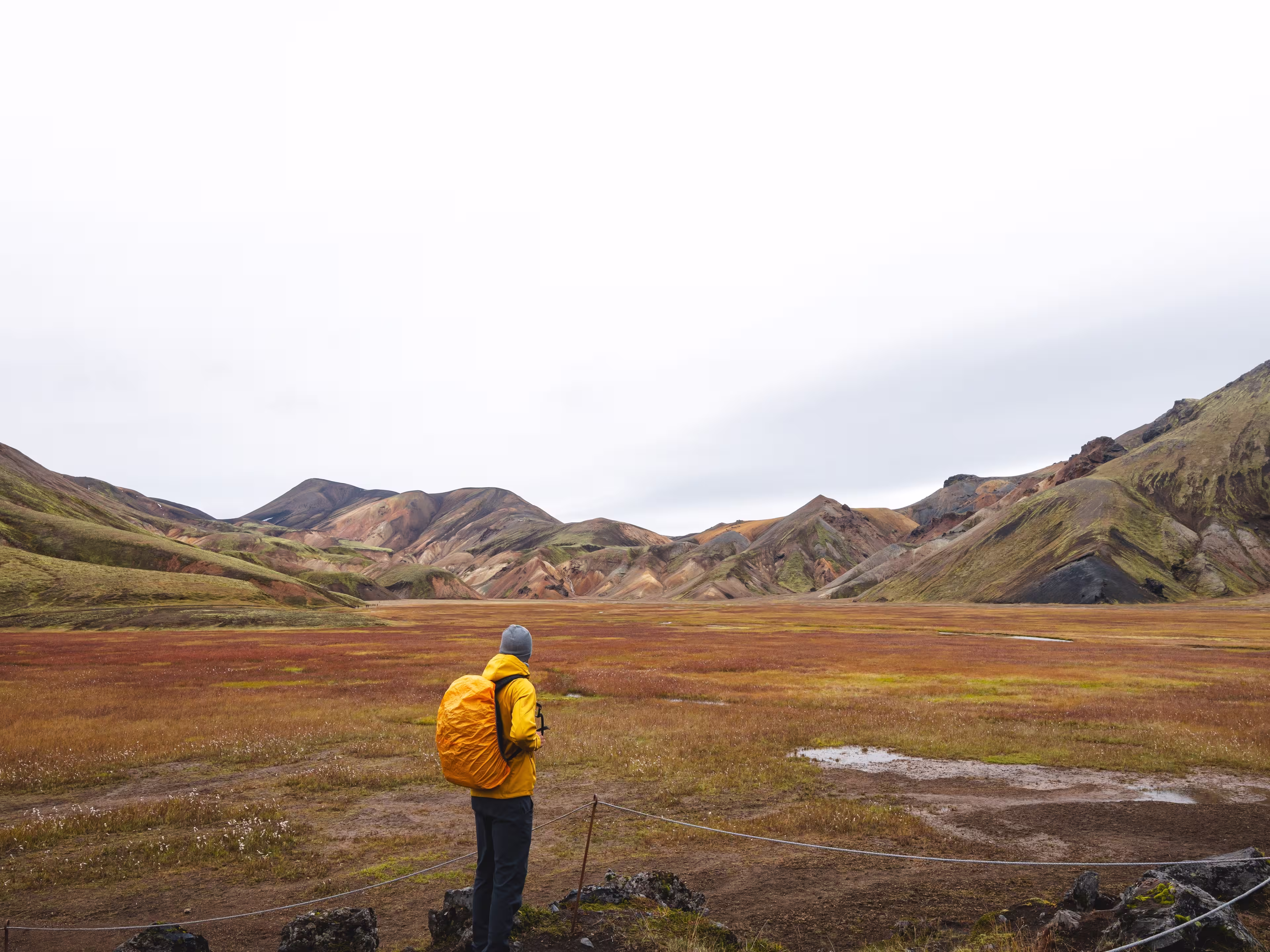 Traveler walks through a rugged lava field in the Icelandic Highlands, surrounded by mossy rocks and distant rhyolite peaks. A surreal journey through Iceland wild heart.
