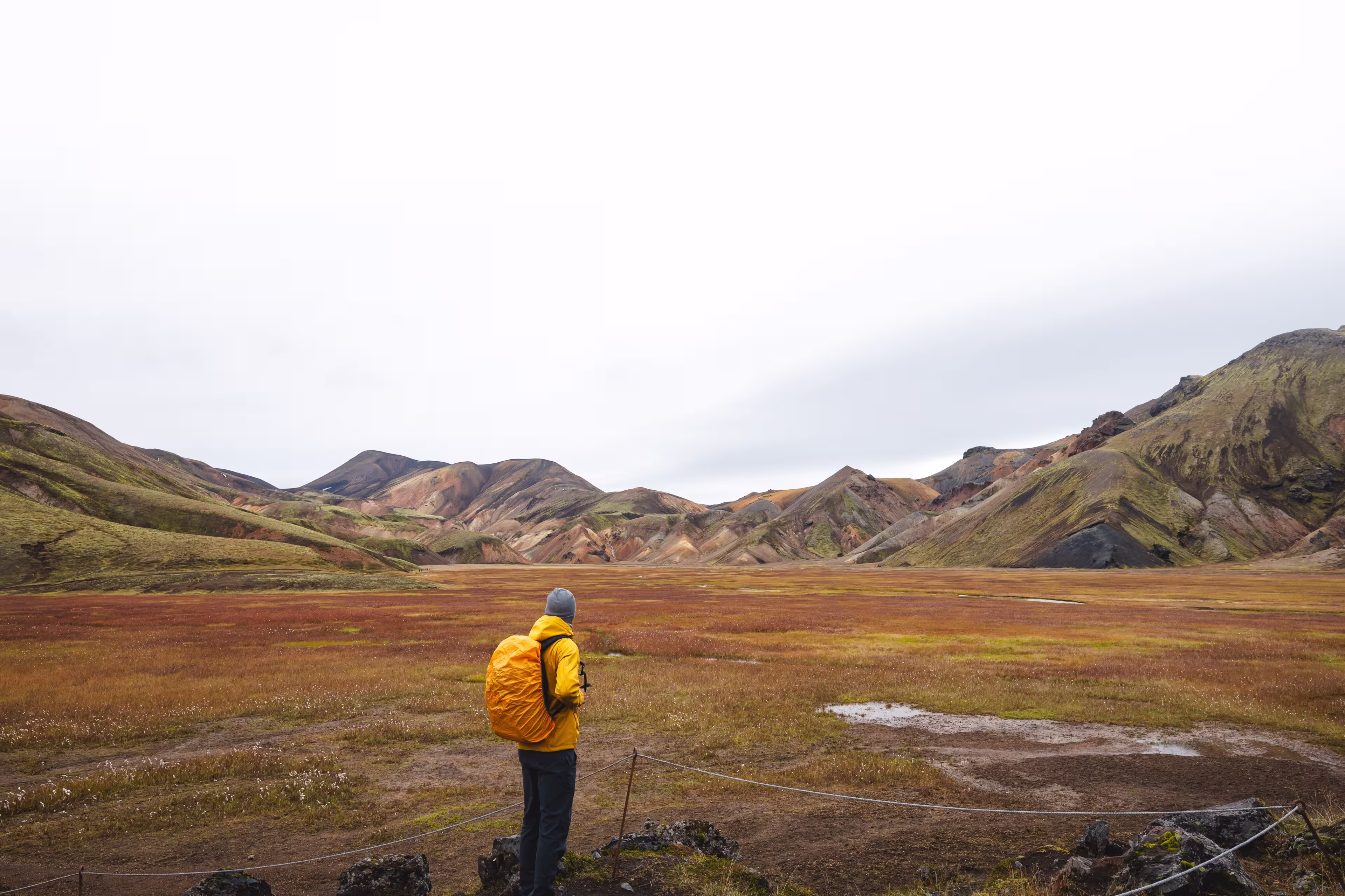 Traveler walks through a rugged lava field in the Icelandic Highlands, surrounded by mossy rocks and distant rhyolite peaks. A surreal journey through Iceland wild heart.