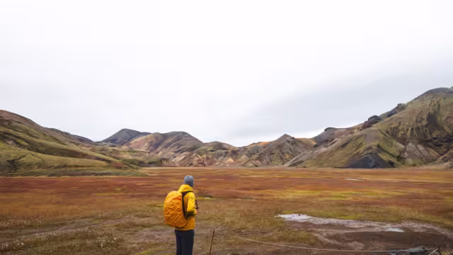 Traveler walks through a rugged lava field in the Icelandic Highlands, surrounded by mossy rocks and distant rhyolite peaks. A surreal journey through Iceland wild heart.