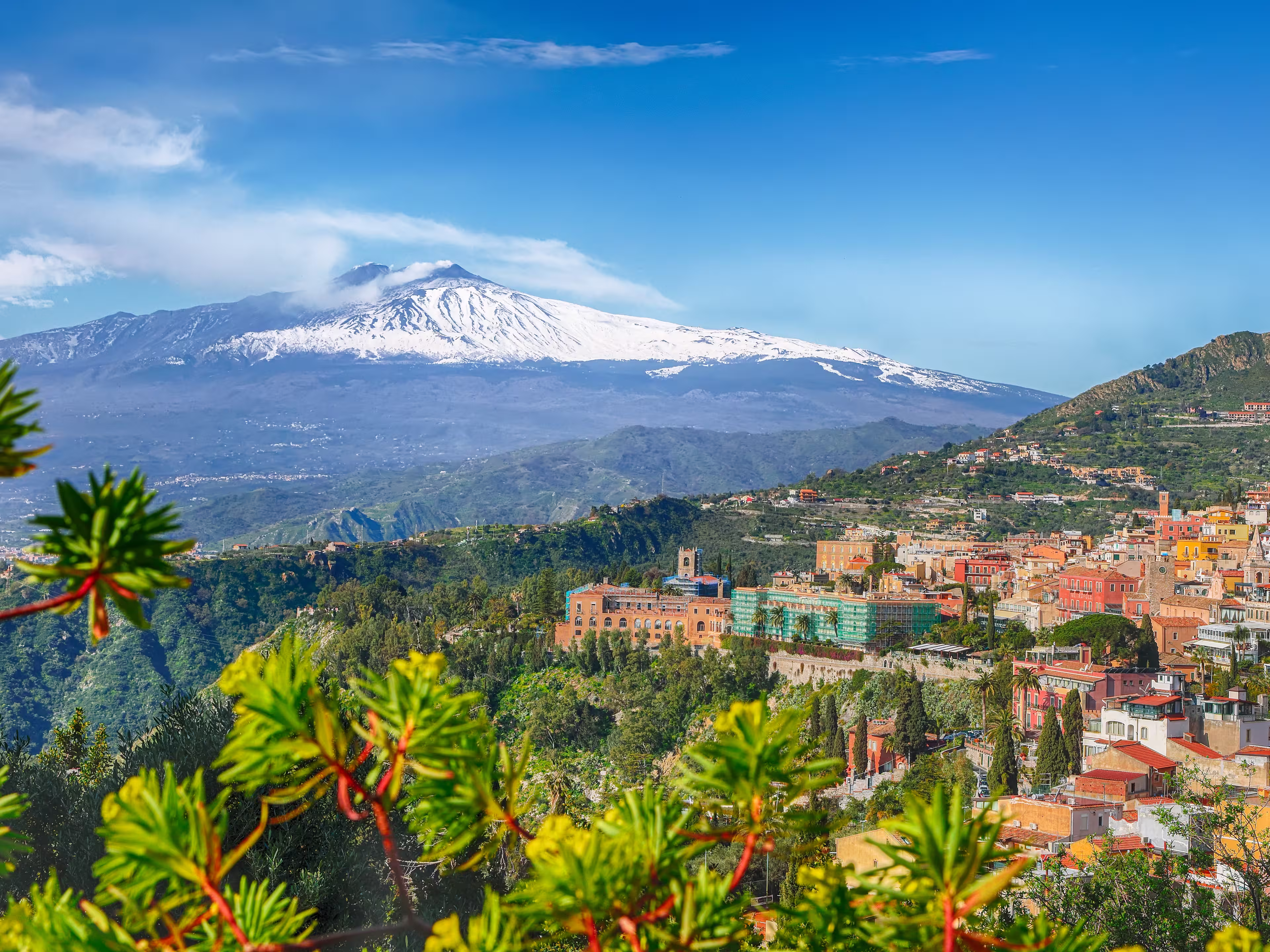 Etna volcano and Taormina town aerial panoramic view. Roofs of a lot of buldings. Smoking snow-capped Mount Etna volcano. Taormina, Sicily, Italy.