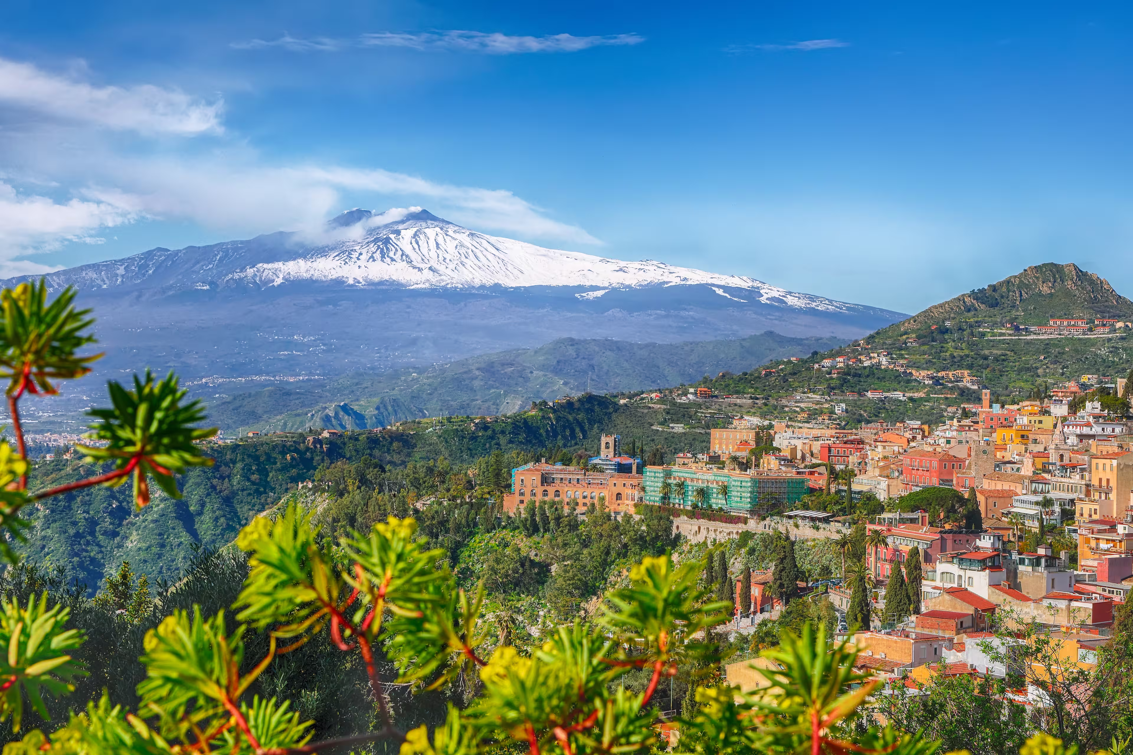 Etna volcano and Taormina town aerial panoramic view. Roofs of a lot of buldings. Smoking snow-capped Mount Etna volcano. Taormina, Sicily, Italy.