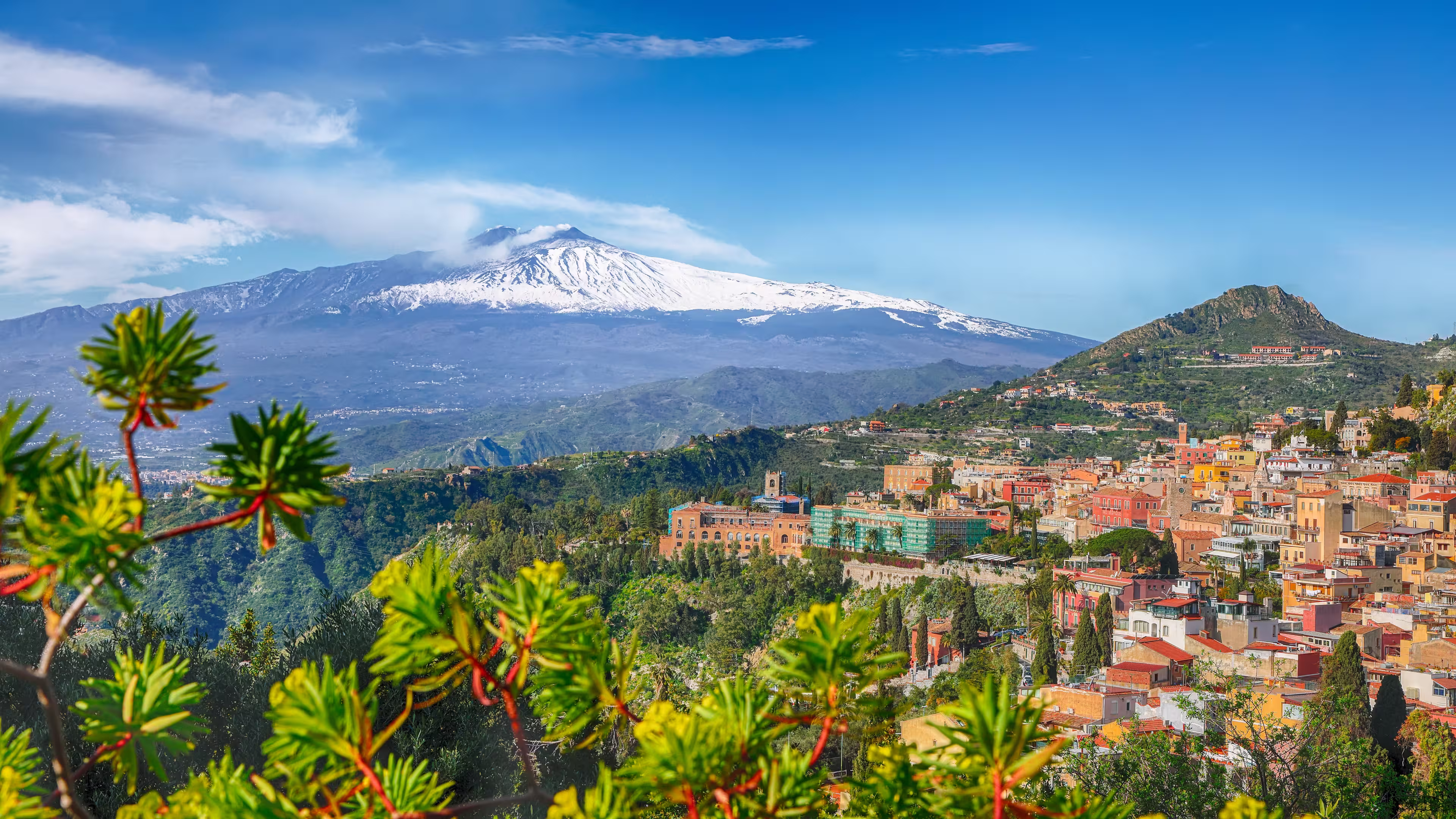 Etna volcano and Taormina town aerial panoramic view. Roofs of a lot of buldings. Smoking snow-capped Mount Etna volcano. Taormina, Sicily, Italy.
