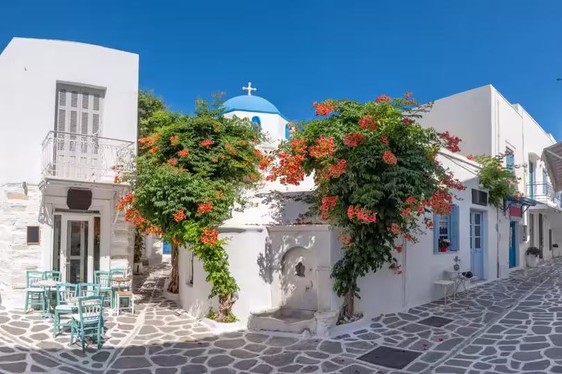 Panorama of the beautiful narrow street in Greece with cozy outdoor cafe and traditional greek church in Parikia town on Paros island, Cyclades
