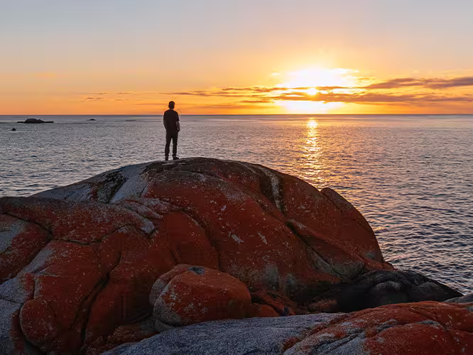 Traveller admiring sunset over the Bay of Fires, Tasmania, Australia