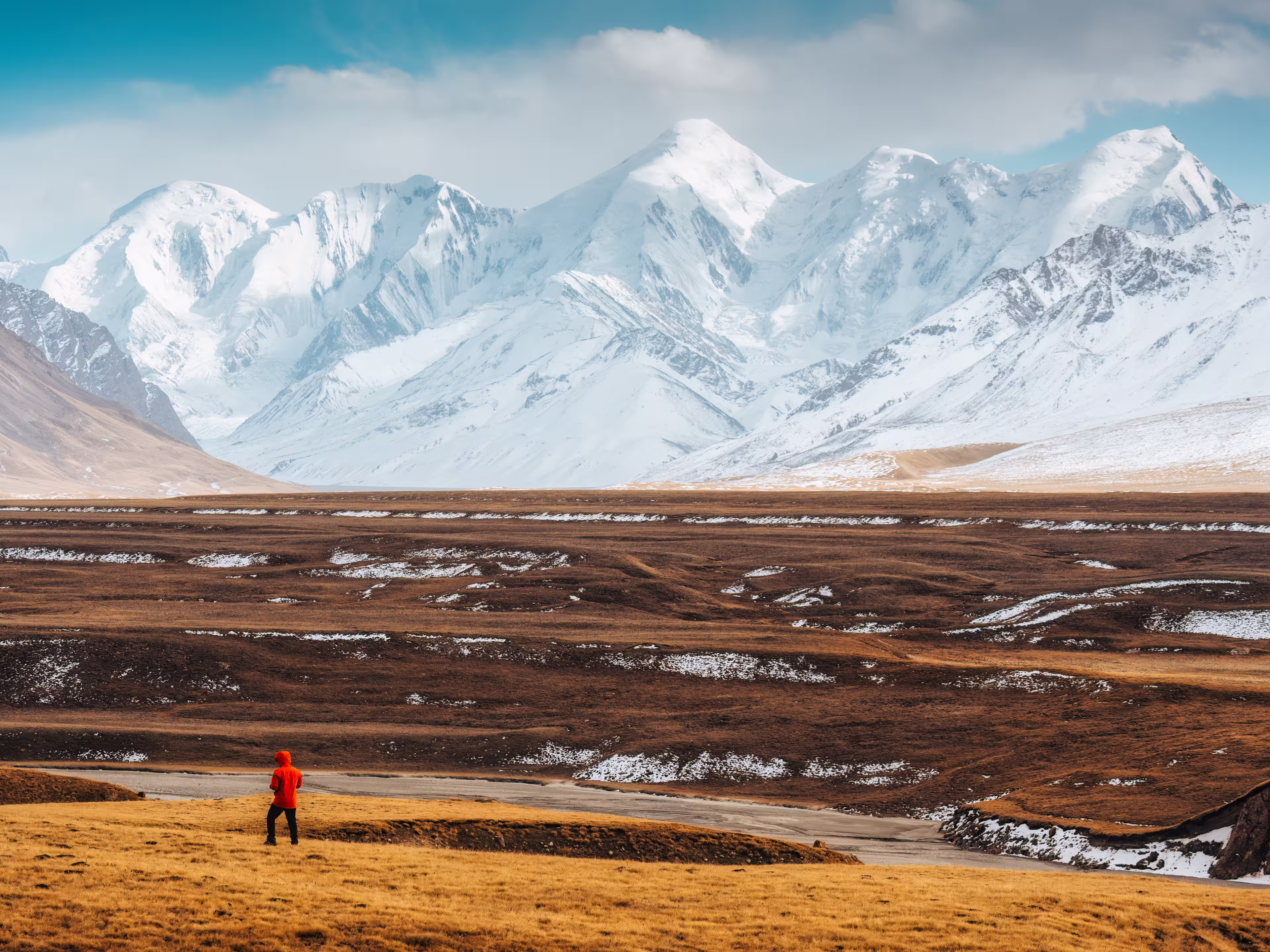 Lone traveler in red jacket facing snowy Tian Shan mountain range on wilderness in autumn at Sary Jaz remote valley, Kyrgyzstan