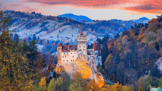 Wide view of medieval Bran Castle during sunset with warm autumn colours of surrounding trees, Transylvania, Romania