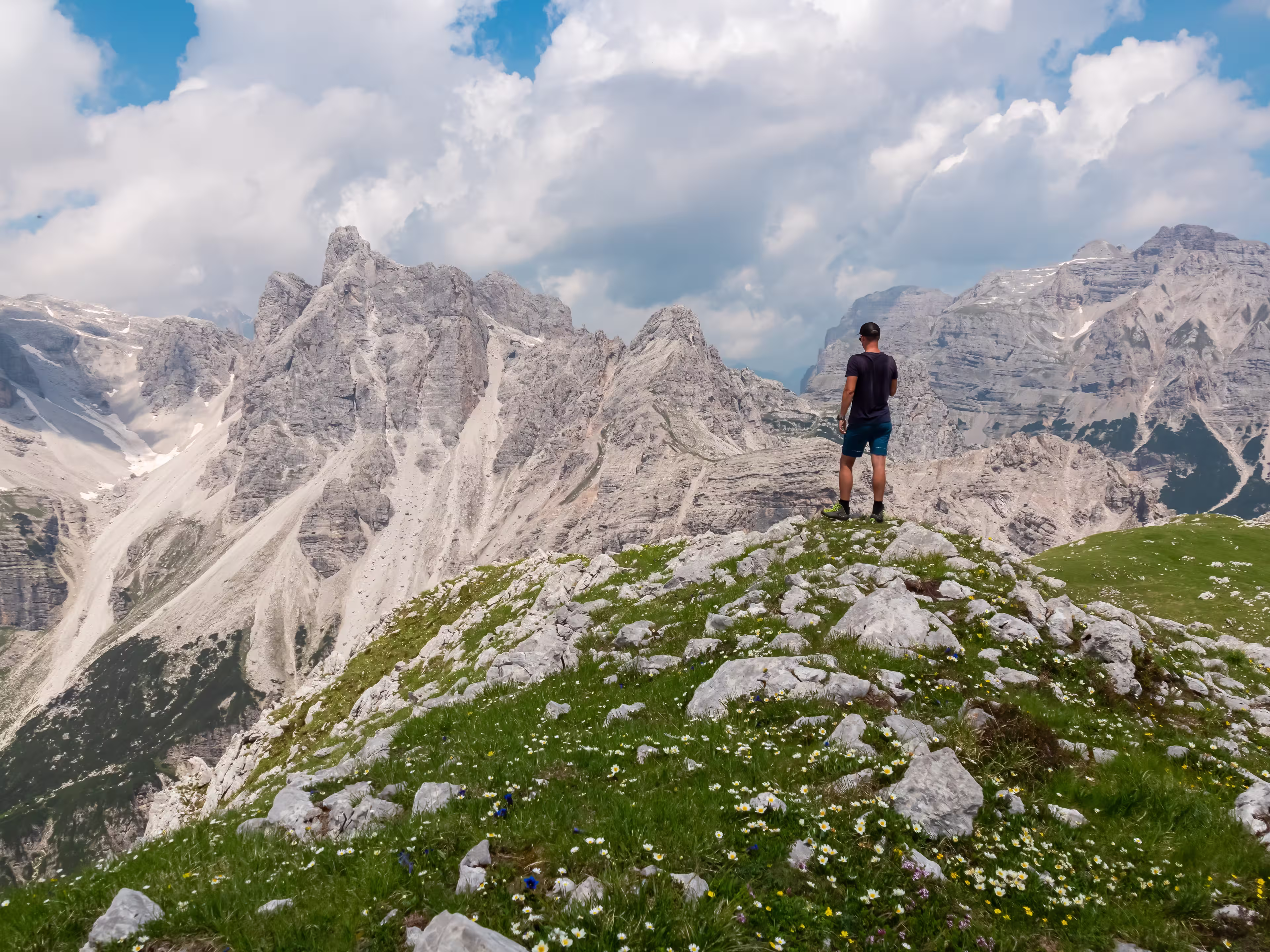 Hiker man on top of Cima Sophia with panoramic view of majestic cloud covered rugged mountain peaks of Brenta Dolomites, Trentino, Italy. Summer wanderlust in alpine wilderness Italian Alps. Freedom