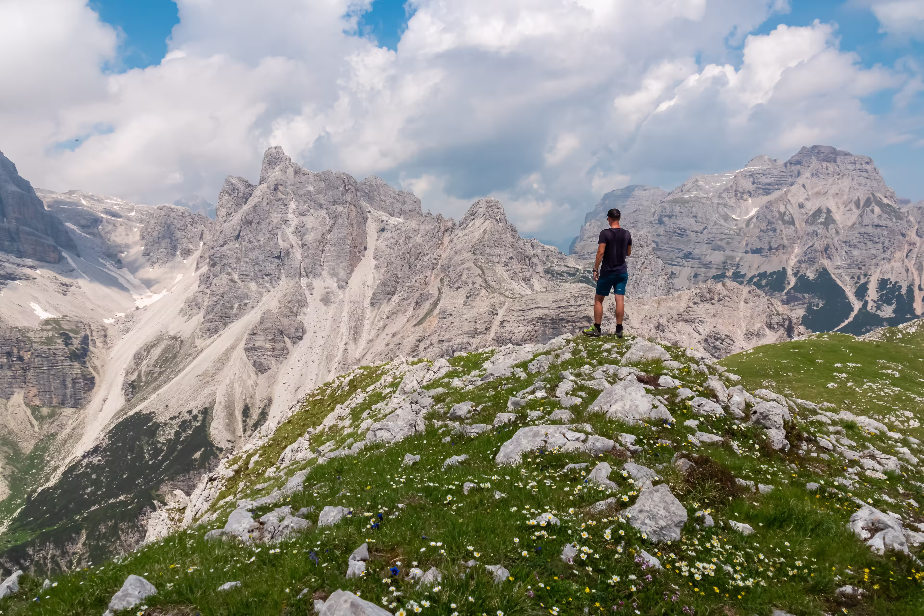 Hiker man on top of Cima Sophia with panoramic view of majestic cloud covered rugged mountain peaks of Brenta Dolomites, Trentino, Italy. Summer wanderlust in alpine wilderness Italian Alps. Freedom
