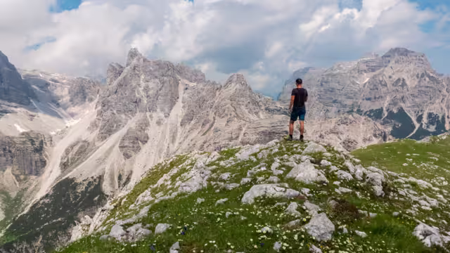 Hiker man on top of Cima Sophia with panoramic view of majestic cloud covered rugged mountain peaks of Brenta Dolomites, Trentino, Italy. Summer wanderlust in alpine wilderness Italian Alps. Freedom
