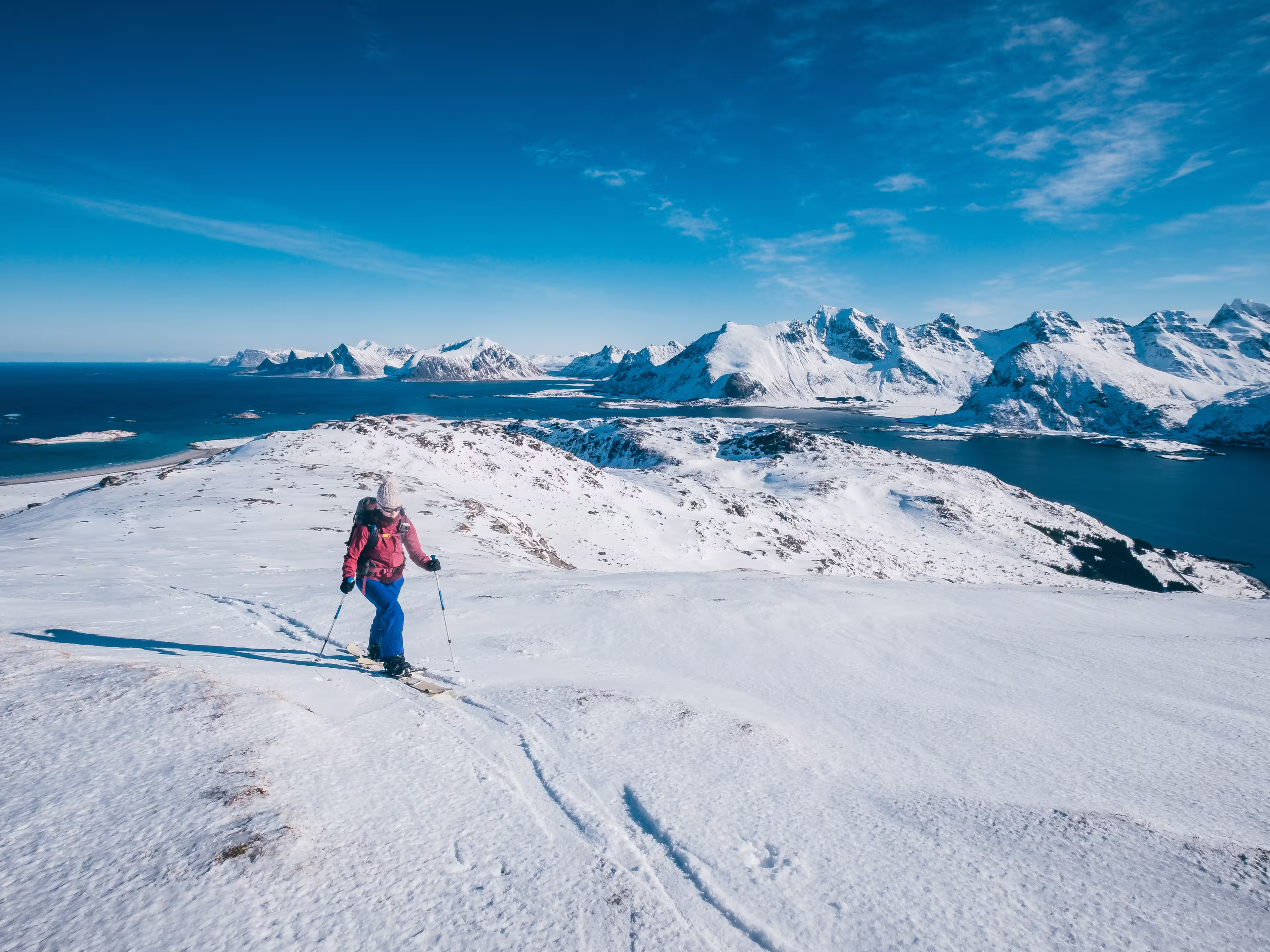Girl skialper reaching the top after a long climb towering over the ocean and the peaks of Lofoten Island