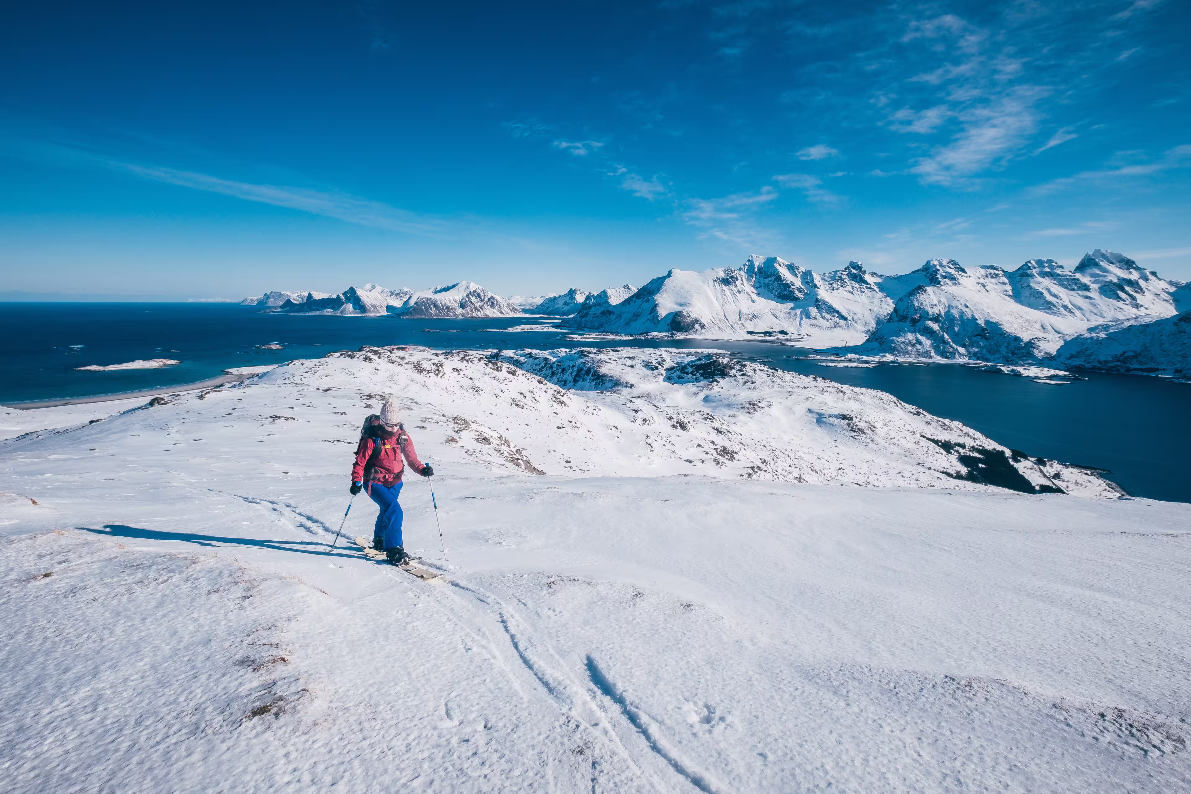 Girl skialper reaching the top after a long climb towering over the ocean and the peaks of Lofoten Island