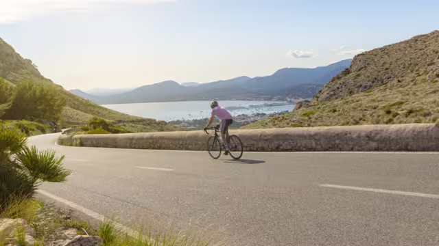 Mallorca Cycling. Cyclist descending a slope towards the port of Pollensa, near the Es Colomer viewpoint in Formentor.