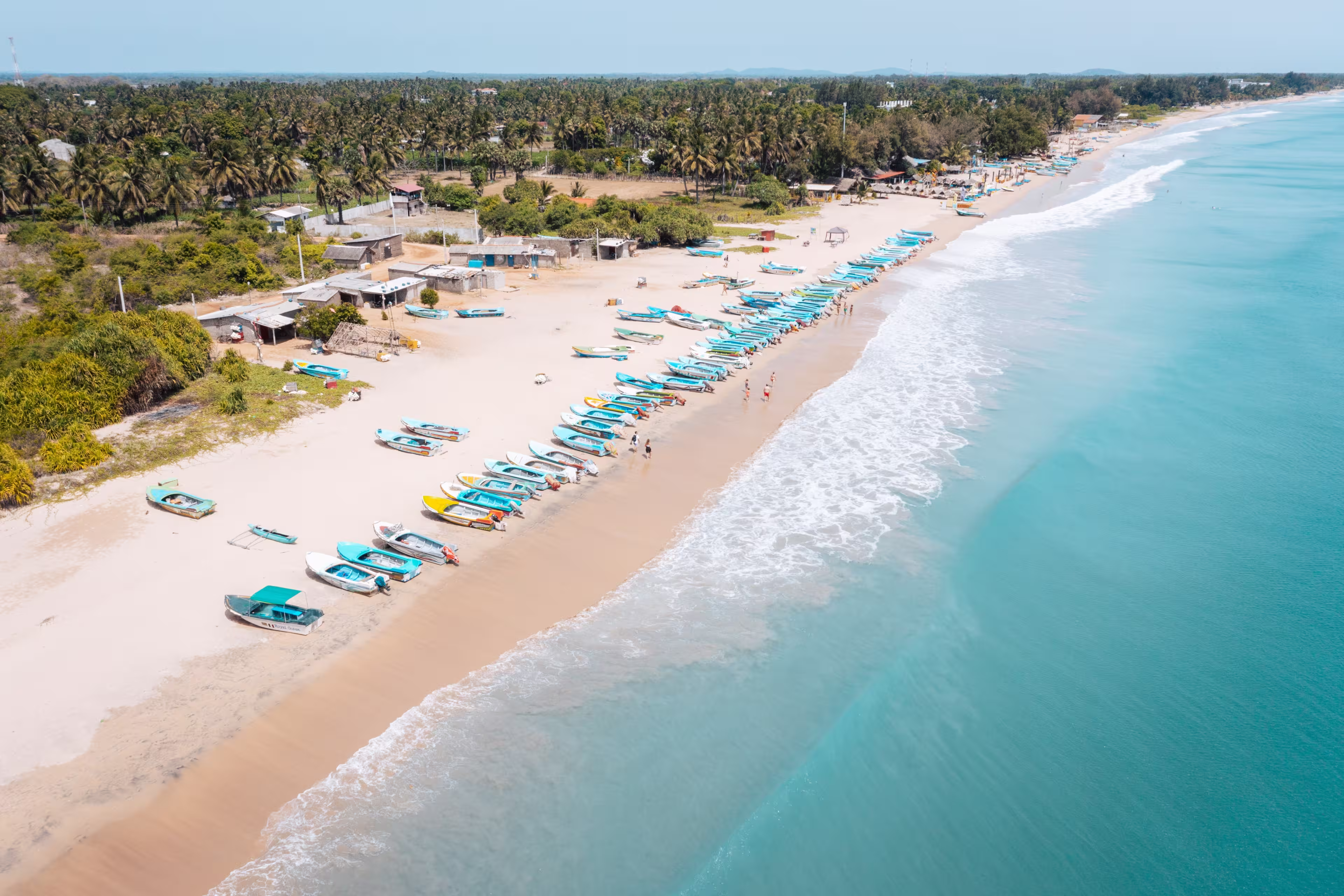 Fishing boats pulled up on sandy shoreline at Nilaveli Beach, Nilaveli, Sri Lanka, with clear turquoise water of the Indian Ocean along the tropical coast.