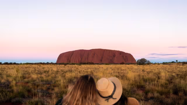 Two Intrepid travellers lean on each other looking out at Uluru in Australia's Red Centre