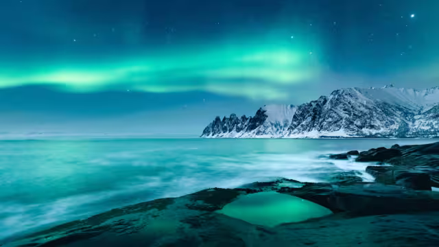 Vivid Northern lights during polar night on Lofoten Islands in Norway. Epic scene of dancing aurora borealis in the night sky over jagged mountain ridge and Arctic ocean on island Senja, polar circle.