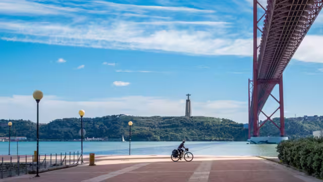 Cyclotourist rides under the April 25 bridge, in Lisbon, Portugal.