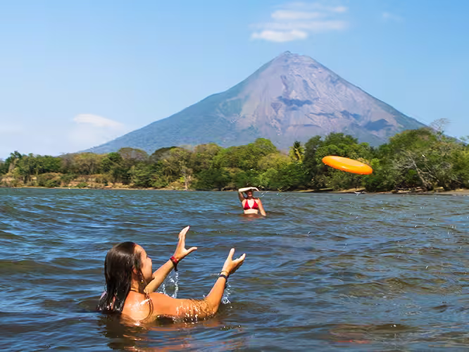 Friends play frisbee in the water in the shadow of volcano Concepcion, Ometepe island, Nicaragua