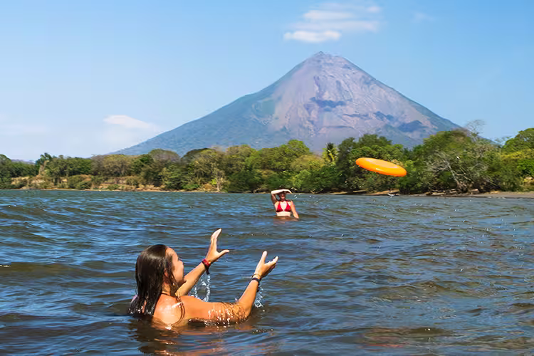 Friends play frisbee in the water in the shadow of volcano Concepcion, Ometepe island, Nicaragua