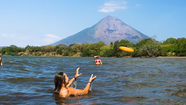Friends play frisbee in the water in the shadow of volcano Concepcion, Ometepe island, Nicaragua