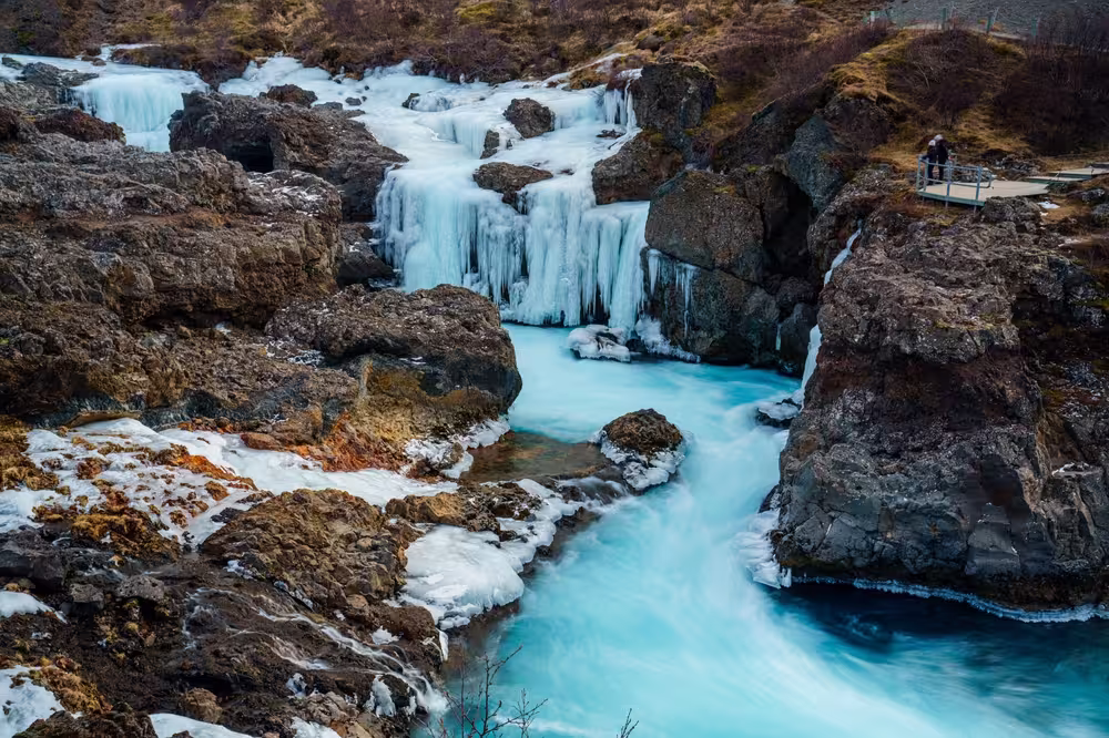 Onlookers view a frozen Barnafoss, or Children’s Falls, a waterfall in West Iceland near Husafell and the Hvita River. Flowing through a narrow rocky gorge in Borgarfjordur.