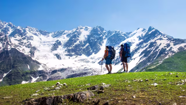Hikers look at mountain range on a sunny summer day. Tourists in the highlands. Hiking in the mountains. Active trip to the beautiful nature. Leisure. Men on mountain trek. People in Caucasus Svaneti