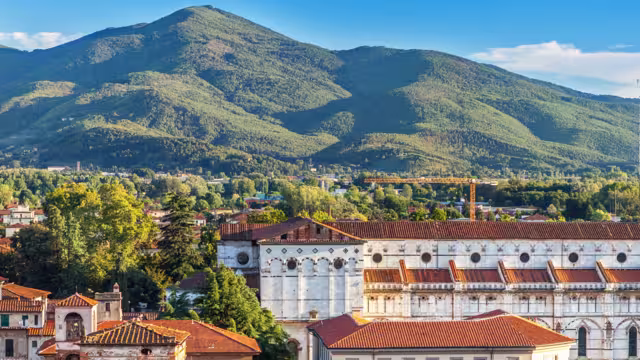Vivid rooftops of old city Lucca with background of colorful green mountains range, Tuscany Italy. Italian ancient cathedral of Saint Martin.