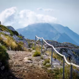 Mountain path on the top of peak Sveti Jure in front of hills and rocks of Biokovo mountain range with cloudy sky, Dalmatia, Croatia