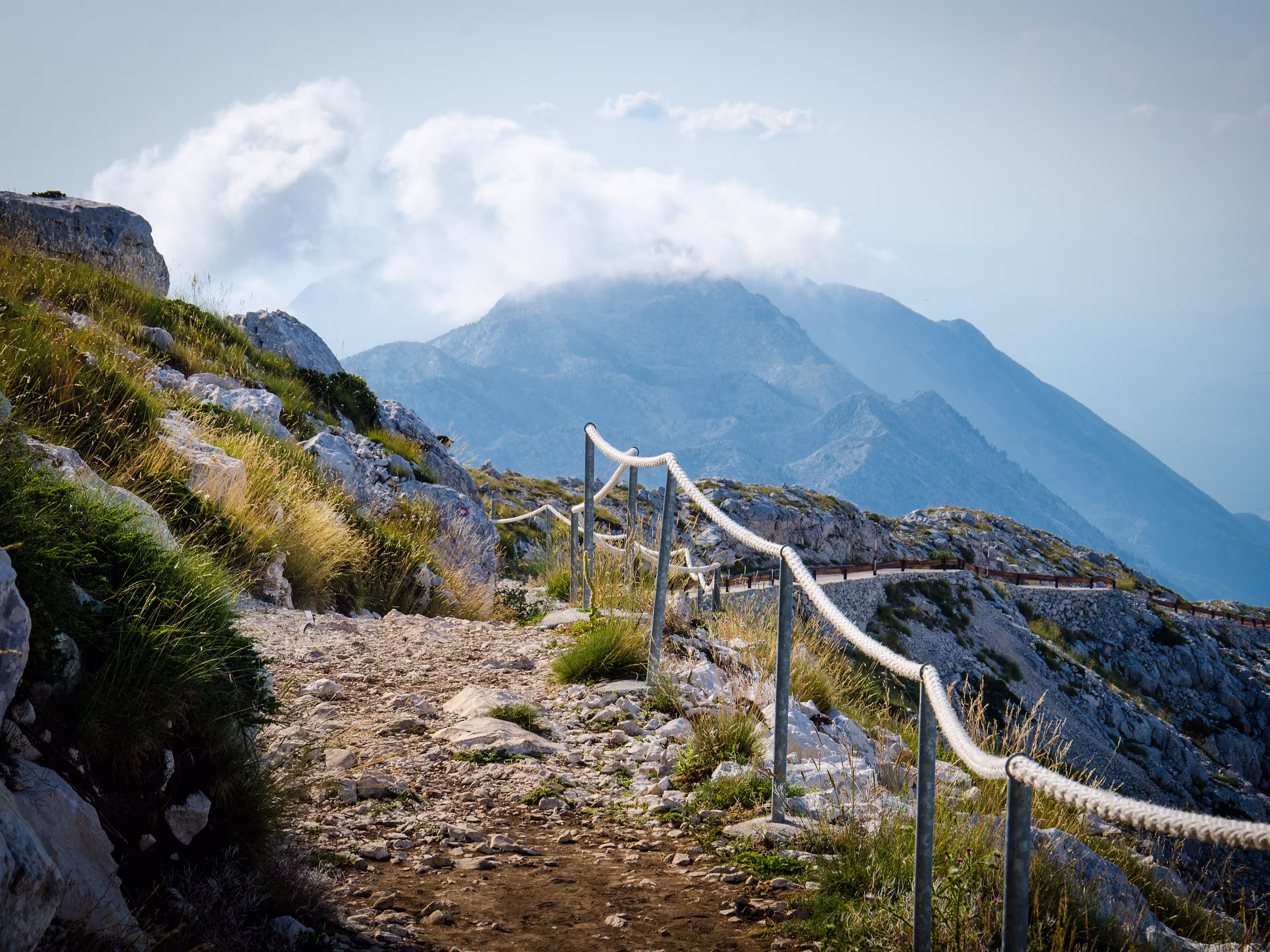 Mountain path on the top of peak Sveti Jure in front of hills and rocks of Biokovo mountain range with cloudy sky, Dalmatia, Croatia
