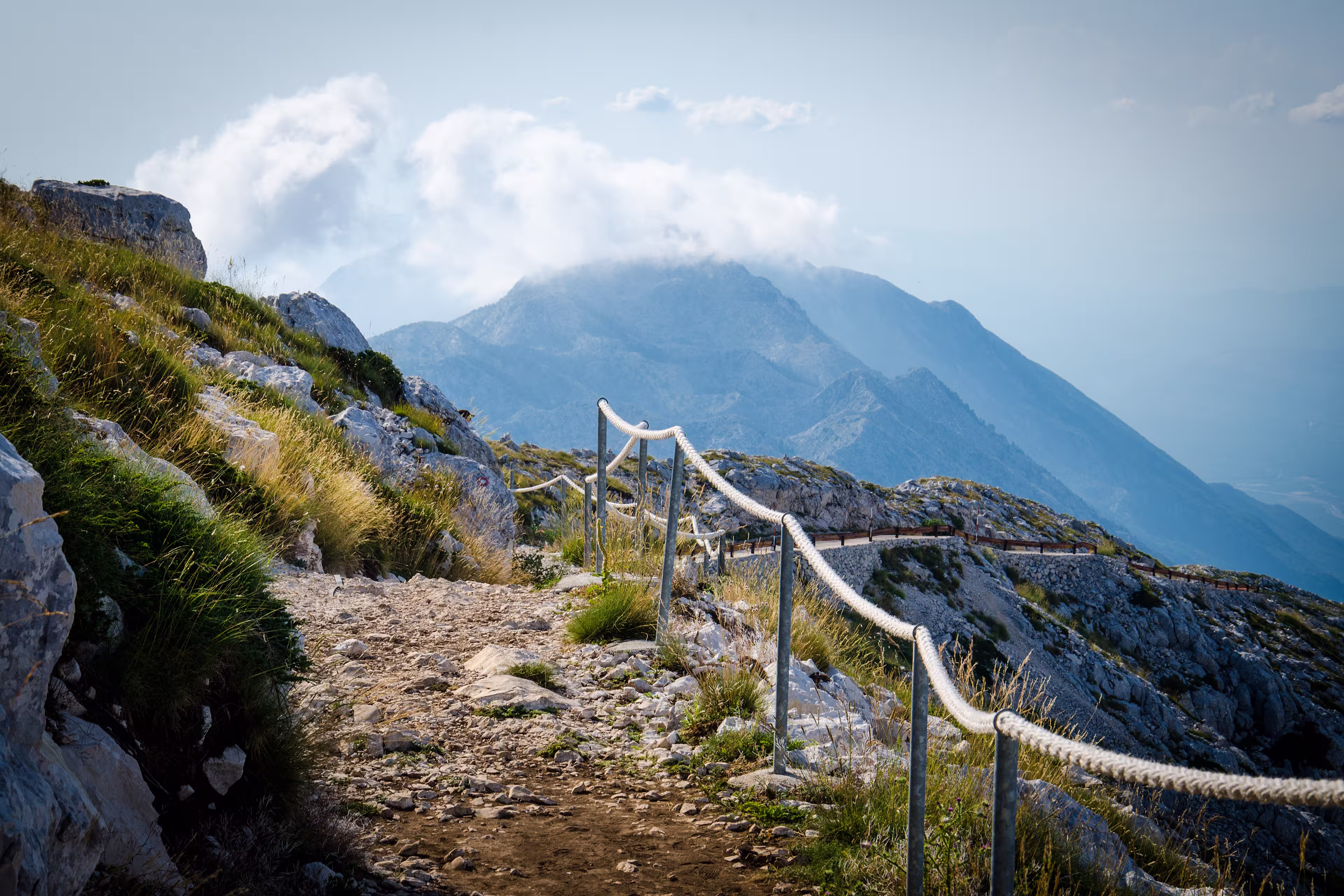 Mountain path on the top of peak Sveti Jure in front of hills and rocks of Biokovo mountain range with cloudy sky, Dalmatia, Croatia