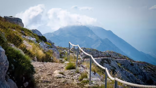 Mountain path on the top of peak Sveti Jure in front of hills and rocks of Biokovo mountain range with cloudy sky, Dalmatia, Croatia