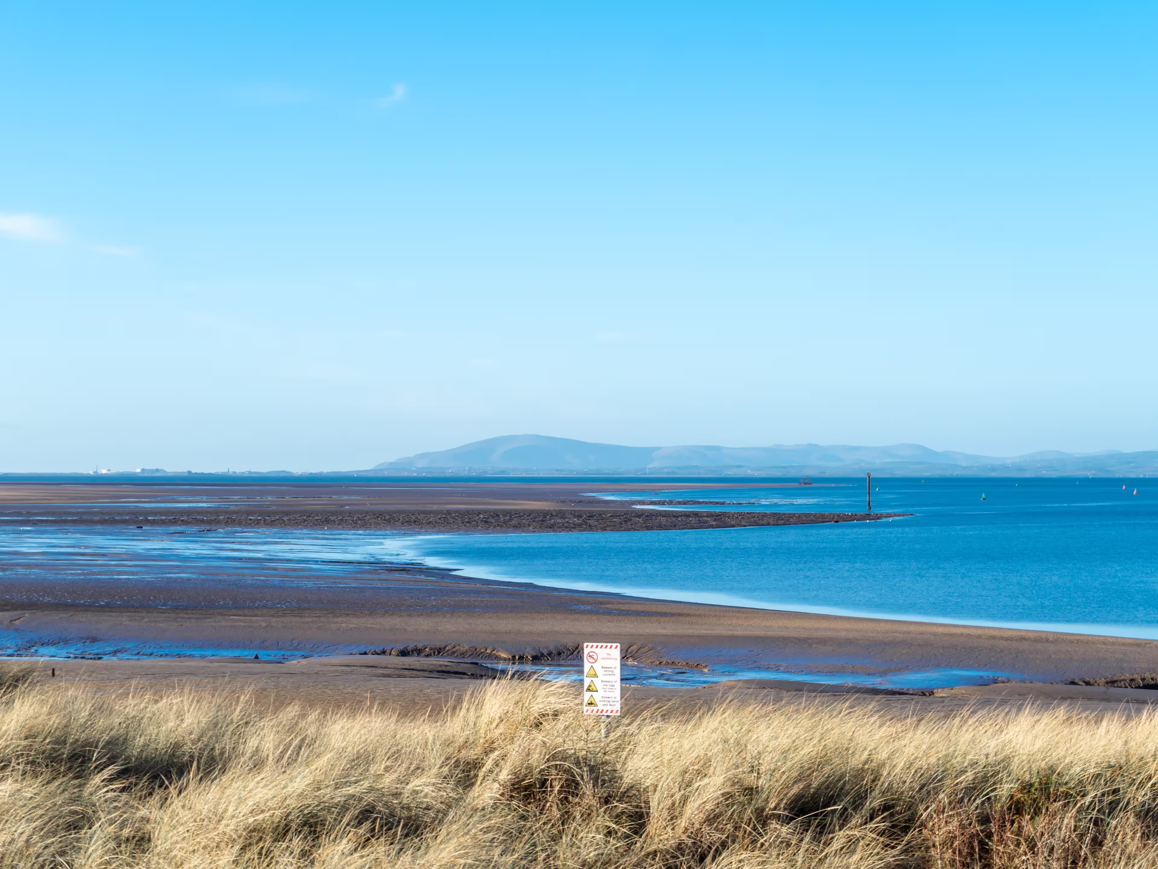 A seascape at low tide with a blue sky, Morecambe Bay. The seashore and the sea against a backdrop of hills on the horizon