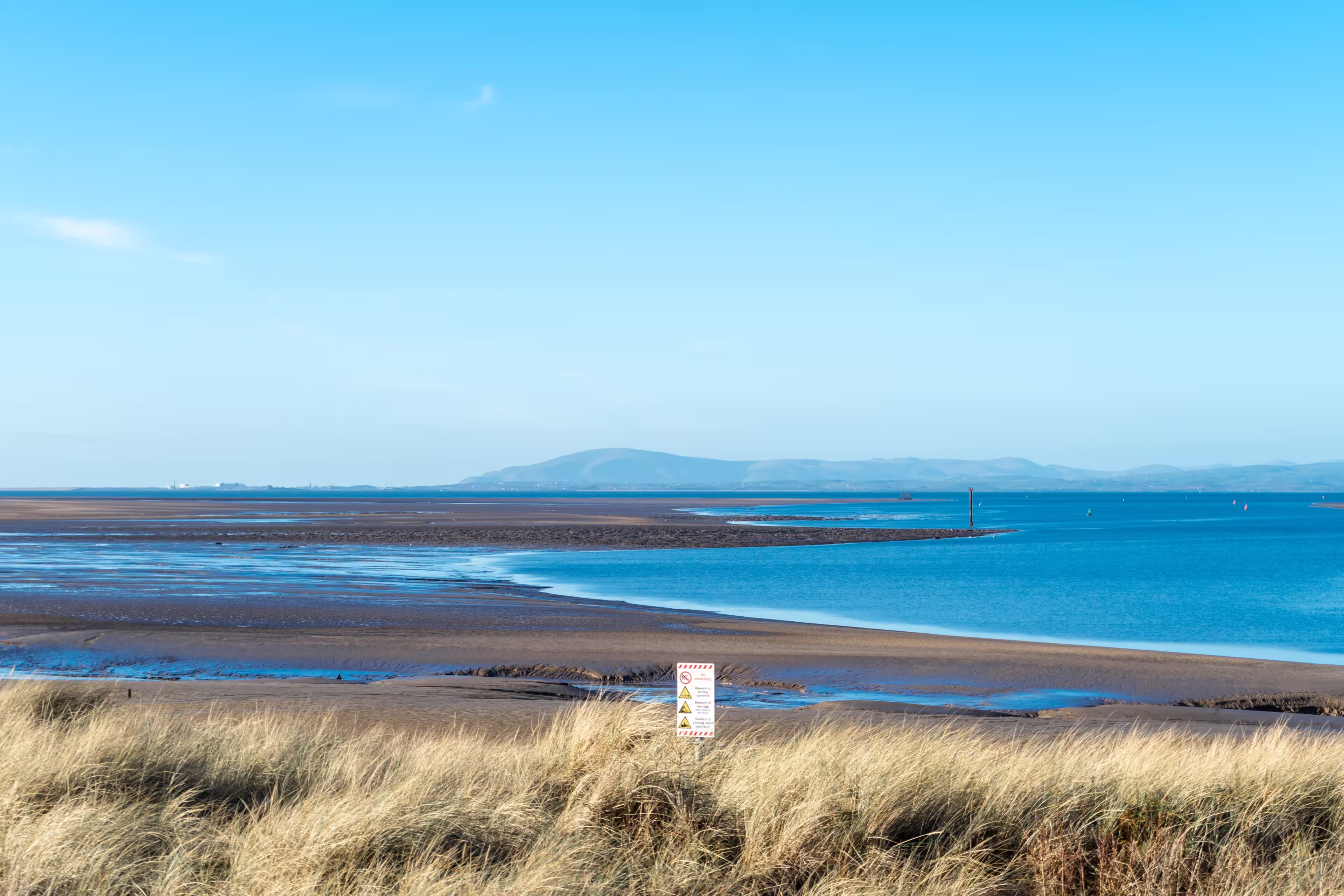 A seascape at low tide with a blue sky, Morecambe Bay. The seashore and the sea against a backdrop of hills on the horizon