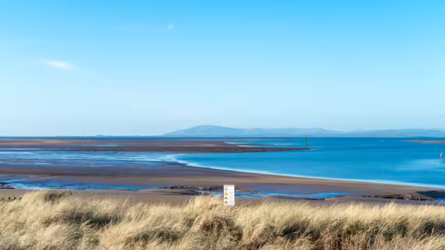 A seascape at low tide with a blue sky, Morecambe Bay. The seashore and the sea against a backdrop of hills on the horizon