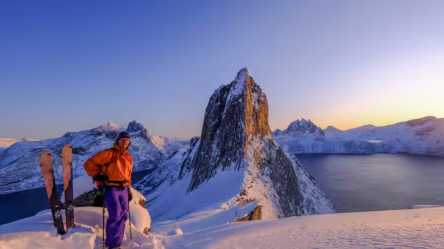Skitouring man standing at the ridge in front of the iconic Segla mountain, view of the ocean fjords, Fjordgard, Senja, Troms, Norway, Europe